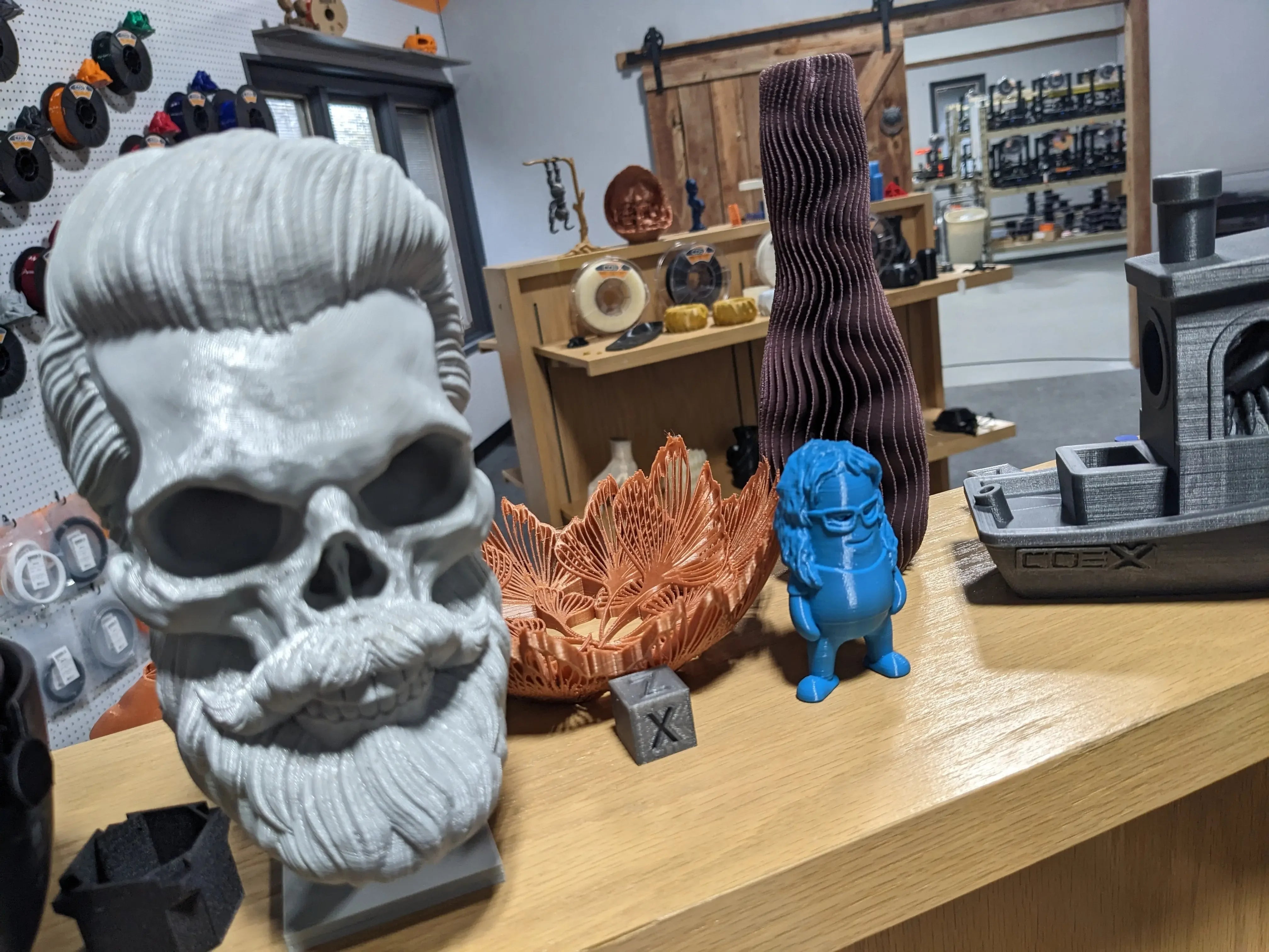 3D printed PLA filament models including skull, vase, flower, boat, and figurine on display