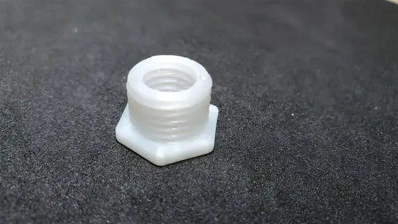 White 3D-printed hex nut made from coextruded nylon PA6 on a black textured surface