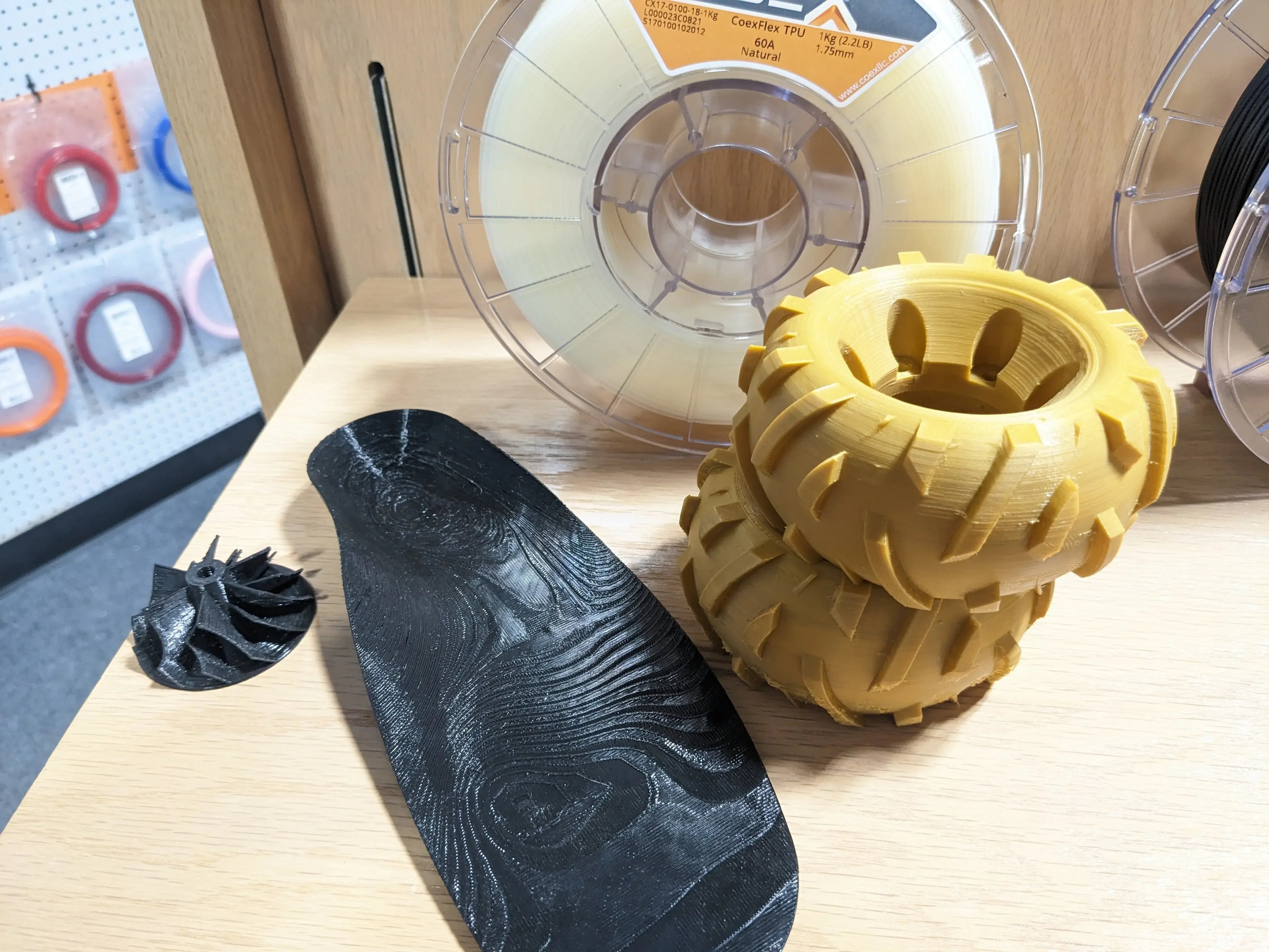 3D printed TPU tires and black parts on a wooden shelf with filament spools in background