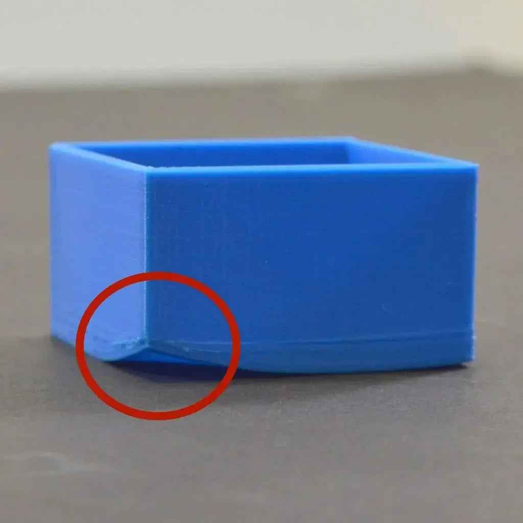 Blue 3D printed ABS box on a gray surface with bed adhesion issue circled in red.