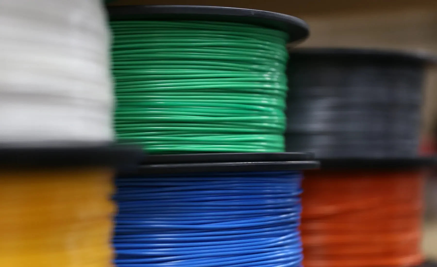 Colorful spools of 3D printer filament including green, blue, white, yellow, black, and orange.