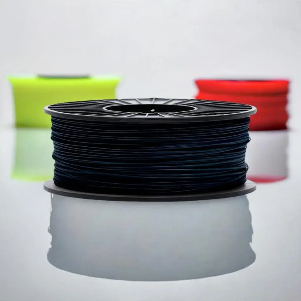 Black 3D printer filament spool on reflective surface with blurred red and yellow spools behind